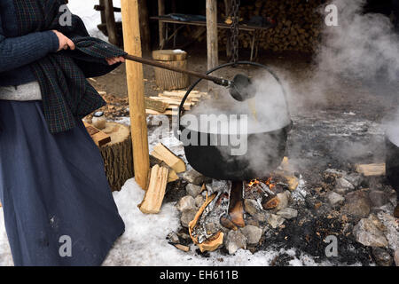 Donna in abiti da Pioneer ladling evaporando sap in ghisa pentola su fuoco di legna per la produzione di sciroppo d'acero in Ontario Canada Foto Stock