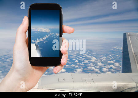 Concetto di viaggio - turistica prendendo foto di nuvole e le terre sotto l'ala del velivolo sul gadget mobile Foto Stock
