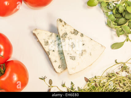 Due triangoli di formaggio blu, tra erbe e pomodori Foto Stock