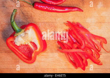 Peperone rosso, peperoncino e pepe fette, su di un tagliere di legno Foto Stock