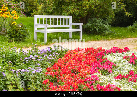 Fiori colorati sull'aiuola di fiori in estate park. White panca in legno sullo sfondo. Messa a fuoco selettiva. Villaggio Trigorskoye, RU Foto Stock