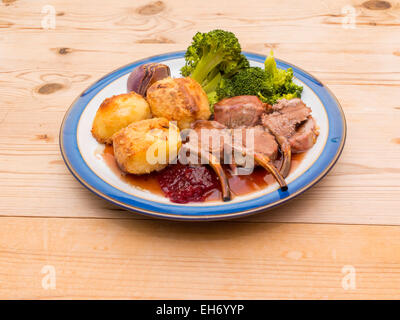 Cena inglese carré d'agnello arrosto broccoli cipolla e sugo di carne servita su un blu e piastra bianca tavolo in legno Foto Stock