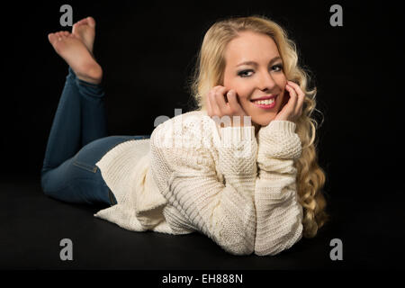 Sorridente giovane donna giacente sul suo stomaco, testa in appoggio nelle sue mani Foto Stock