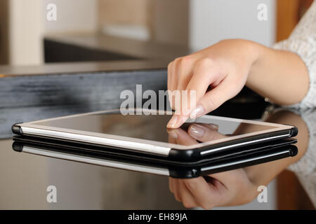 Donna mano premendo un tablet touch screen su una tavola a casa Foto Stock