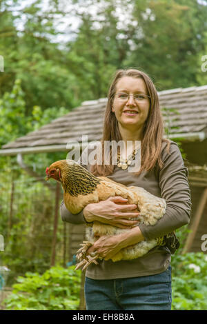 Donna che mantiene un Buff Brahma hen, con un custom-costruito pollaio sullo sfondo, in Issaquah, Washington, Stati Uniti d'America Foto Stock