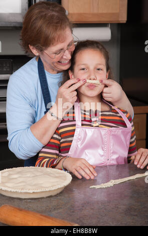 Nonna scherzosamente tenendo su una base di pastafrolla per torta pezzo che è stato rifilato dalla torta in parte anteriore del nipote del volto Foto Stock