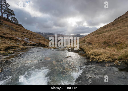 Stream tumbling giù da Mount Snowdon, Snowdonia, Galles; mountain range sull orizzonte con raggi del sole proveniente attraverso il cloud. Foto Stock