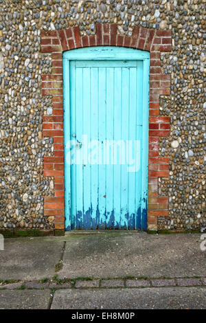 Una porta blu turchese in una tradizionale parete di pietra focaia, ciottoli e mattoni ad Aldeburgh, Suffolk, Regno Unito Foto Stock