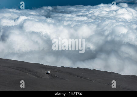 La guida in salita su strada di lava al vulcano Etna con le nuvole in background Foto Stock