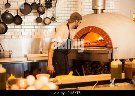 Lo chef posizionando la pizza in un tradizionale forno a mattoni, industriale mangia, Buellton, California Foto Stock