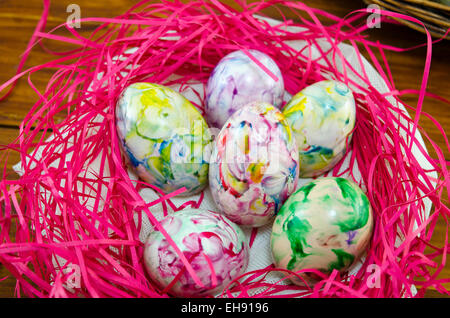 Colorato e dipinto di uova in un nido di rosa su una tavola di legno Foto Stock