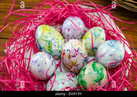 Colorato e dipinto di uova in un nido di rosa su una tavola di legno Foto Stock