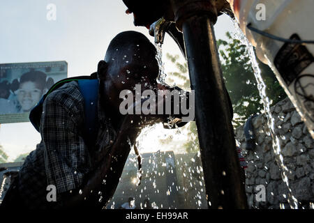 Un uomo haitiano bevande acqua sicura da un pubblico pompa acqua a Port-au-Prince, Haiti. Foto Stock