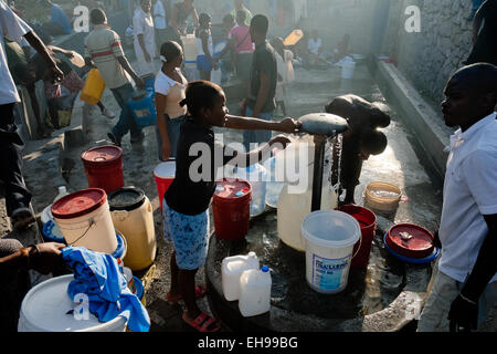 Una ragazza haitiana riempie i barili di plastica con acqua potabile sicura da un pubblico pompa acqua a Port-au-Prince, Haiti. Foto Stock