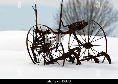 Un pezzo di antiquariato di attrezzature agricole siede scartati nella neve. Foto Stock