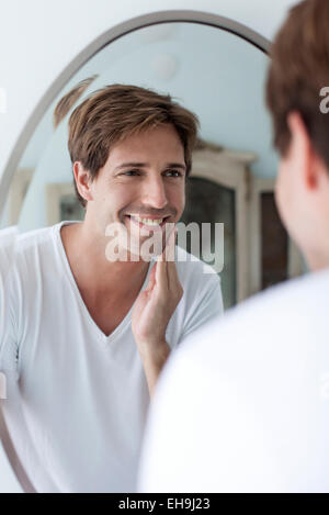 Uomo che guarda a sé nel mirror ammirando stoppia del viso Foto Stock