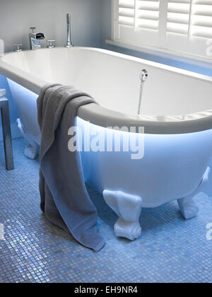 Moderno illuminato blu vasca da bagno con vasca da bagno in ceramica piedi e pavimento a mosaico dettaglio in Fernhurst Road home, REGNO UNITO Foto Stock