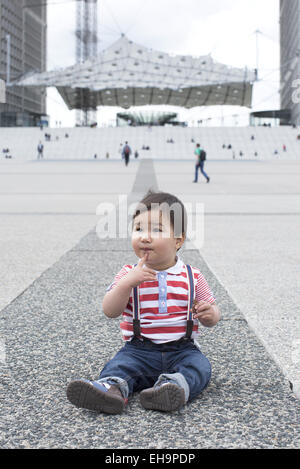 Bambino seduto per terra in piazza della città Foto Stock