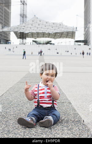 Bambino seduto per terra in piazza della città Foto Stock