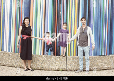 Famiglia tenendo le mani insieme di fronte a strisce colorate sculture, La Defense, Parigi, Francia Foto Stock