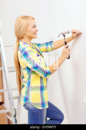 Donna sorridente martellamento chiodo nella parete Foto Stock