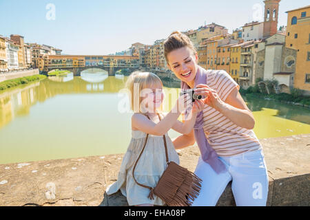 Felice madre e bambina controllare le foto nella fotocamera sul ponte che si affaccia su ponte vecchio a Firenze, Italia Foto Stock