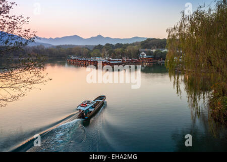 Cinese piccola barca da pesca con barcaiolo va al lago occidentale costa. Famoso Parco in Hangzhou city centre, Cina Foto Stock