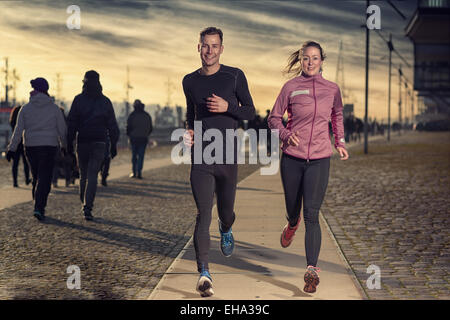 Fit active coppia giovane in esecuzione su un lungomare con la donna atletica portando il modo avvicinando la fotocamera Foto Stock