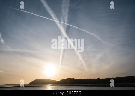 Ferryside, UK. 10 marzo, 2015. Aeroplano vapore sentieri di vapore attraverso il cielo dal villaggio di Ferryside al tramonto. Il castello di Llanstephan silhouette sul fiume Towy. Credito: Paolo Quayle/Alamy Live News Foto Stock