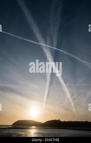 Ferryside, UK. 10 marzo, 2015. Aeroplano vapore sentieri di vapore attraverso il cielo dal villaggio di Ferryside al tramonto. Il castello di Llanstephan silhouette sul fiume Towy. Credito: Paolo Quayle/Alamy Live News Foto Stock