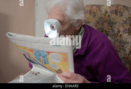 Donna anziana affetti da degenerazione maculare senile usando un dispositivo per aiutare il suo letto piccolo giornale stampare Foto Stock
