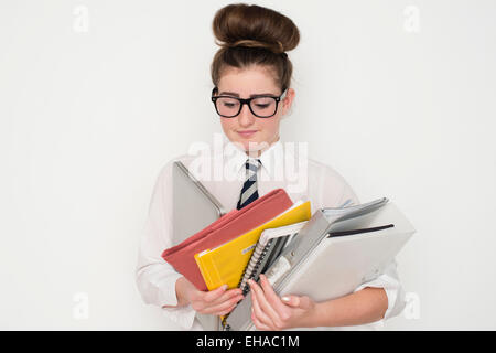 Un gravati oberati di lavoro 13 14 15 anno vecchio geek geeky da stupidi schoolgirl portando una pila di esercitare i notebook e i compiti di scuola corsi di file con gli occhiali e un'uniforme scolastica REGNO UNITO Foto Stock