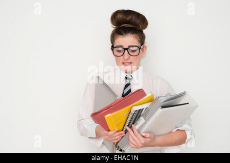 Un gravati oberati di lavoro 13 14 15 anno vecchio geek geeky da stupidi schoolgirl portando una pila di esercitare i notebook e i compiti di scuola corsi di file con gli occhiali e un'uniforme scolastica REGNO UNITO Foto Stock