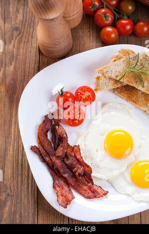 Uova fritte e pancetta affumicata su una piastra con spezie e verdure. Studio shot Foto Stock