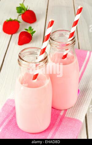 Fragola il latte in bottiglie tradizionali con cannucce su bianco tavola di legno Foto Stock