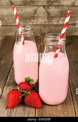 Fragola il latte in bottiglie tradizionali con cannucce su uno sfondo di legno vecchio Foto Stock