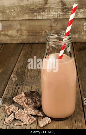 Cioccolato al latte in bottiglia tradizionale con paglia su uno sfondo di legno vecchio Foto Stock