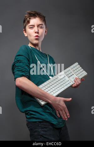 Ragazzo adolescente utilizzando la tastiera del computer come una chitarra, isolato su grigio Foto Stock