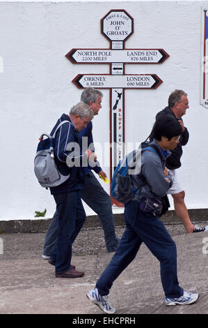 Walkers passando il segno indicante le distanze di Land's End, John O'Semole, Caithness in Scozia Foto Stock