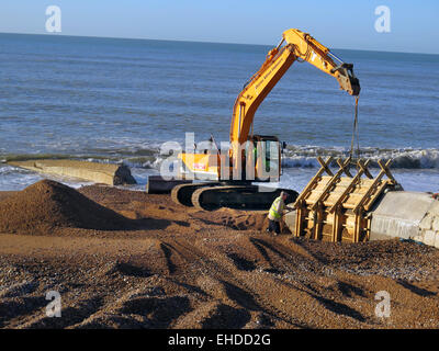 Un escavatore Caterpillar e Thorne Ingegneria Civile preparare i lavoratori per rimuovere lo stampaggio in legno da nuovi pennelli di calcestruzzo essendo costruito sulla spiaggia di Hove, East Sussex. Foto Stock