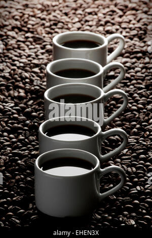 Bianco tazze di caffè in fila su di chicchi di caffè Foto Stock