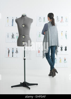 Femmina designer di moda in piedi nel suo studio guardando gli schizzi Foto Stock