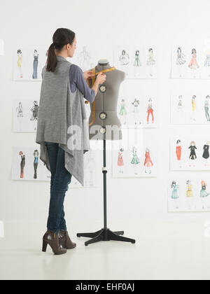 Giovane femmina caucasica designer di moda misure sul manichino nel suo studio Foto Stock