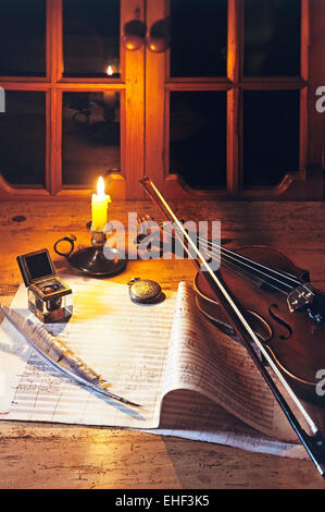 Violino su di un foglio di musica con inkwell e quill, illuminata da una candela Foto Stock