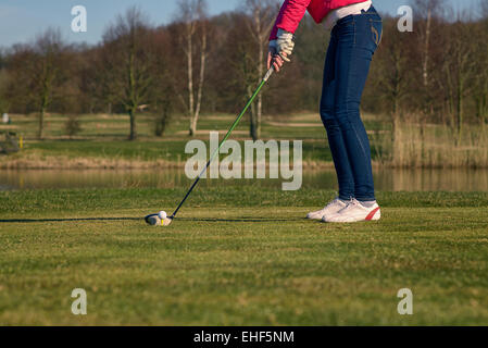 Donna di rinvio su un campo da golf in piedi nella scatola a t di fronte a un pericolo in acqua con un autista nelle sue mani pronto a tee-off Foto Stock