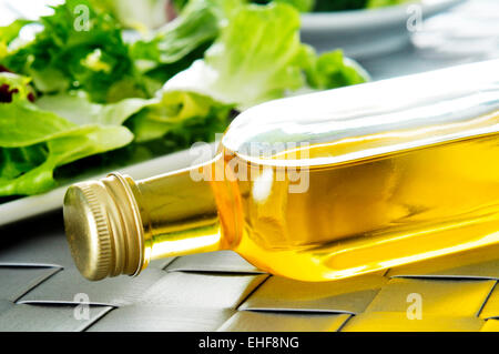 Primo piano della bottiglia di dell'olio d'oliva spagnolo su un set table, con una piastra con lattuga in background Foto Stock