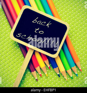 Frase torna a scuola scritto in una etichetta di blackboard e alcune matite di diversi colori di sfondo verde, con un Foto Stock