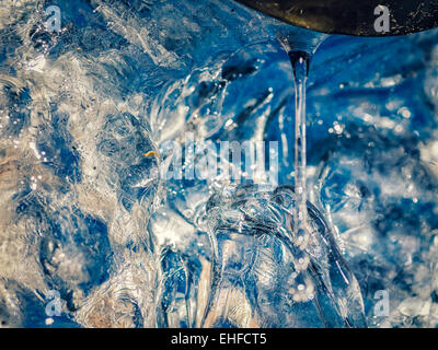 Goccia di ghiaccio fondente acqua al tubo di drenaggio, con il colore blu del cielo blu passando attraverso. Foto Stock