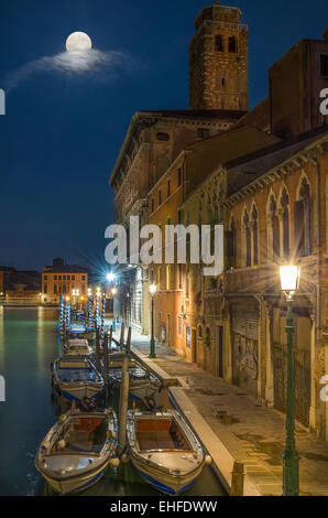 Barche ancorate a venezia canal, strada illuminata da lampade e luna piena, con mobili nuvole, verde acqua riflessione Foto Stock