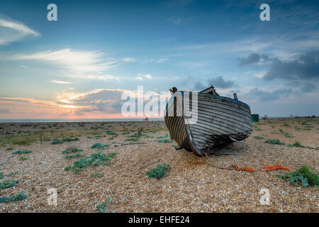 Un bel vecchio weathered legno barca di pesca su una spiaggia di ciottoli di sunrise Foto Stock